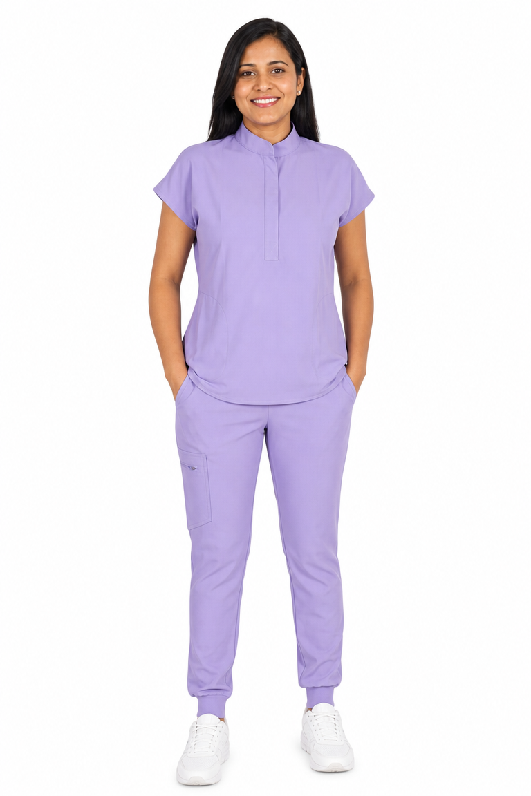 A woman modeling a matching lavender purple scrub set consisting of a short-sleeve mock-neck top and jogger pants, paired with white sneakers, against a plain white background.