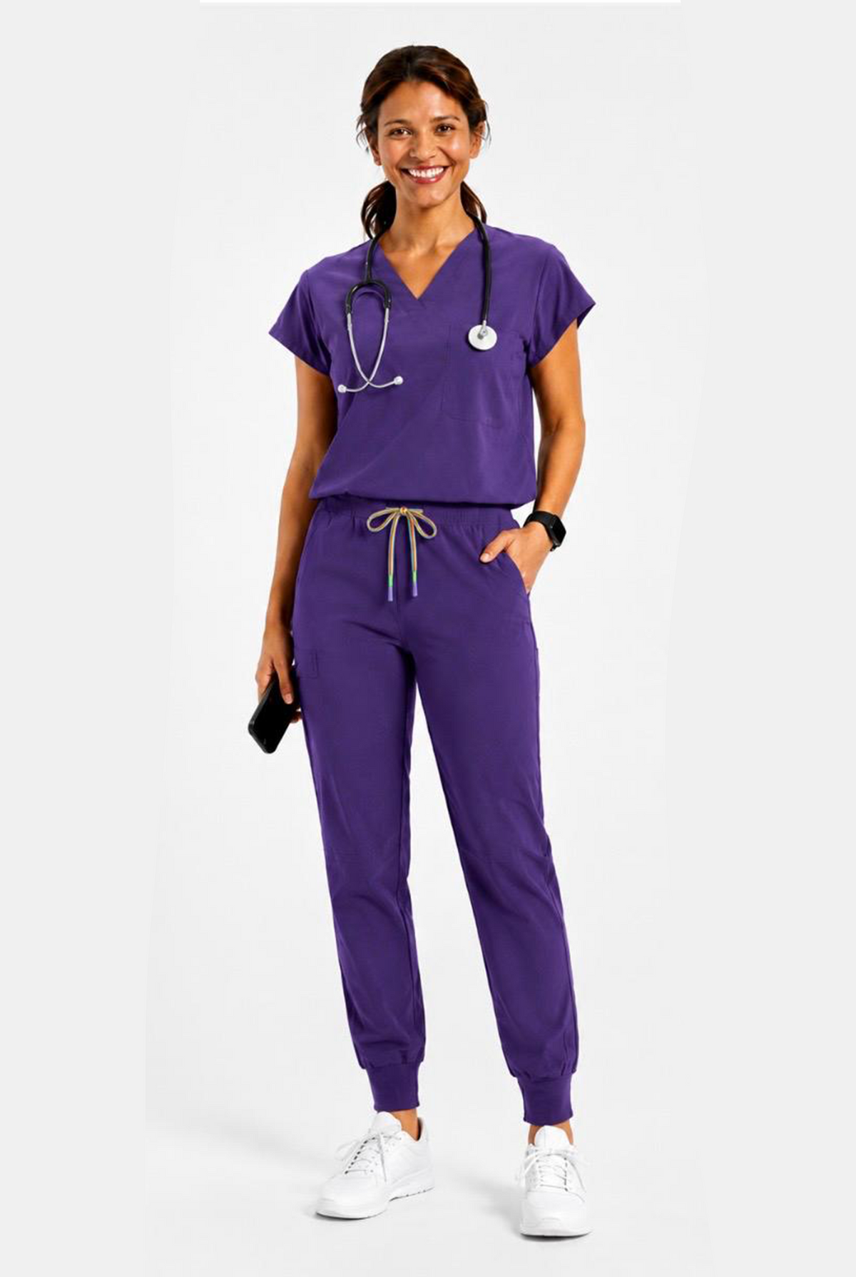 A woman modeling a matching purple medical scrub set consisting of a short-sleeve V-neck top and jogger pants, with a stethoscope around her neck and white sneakers, against a light gray studio background.