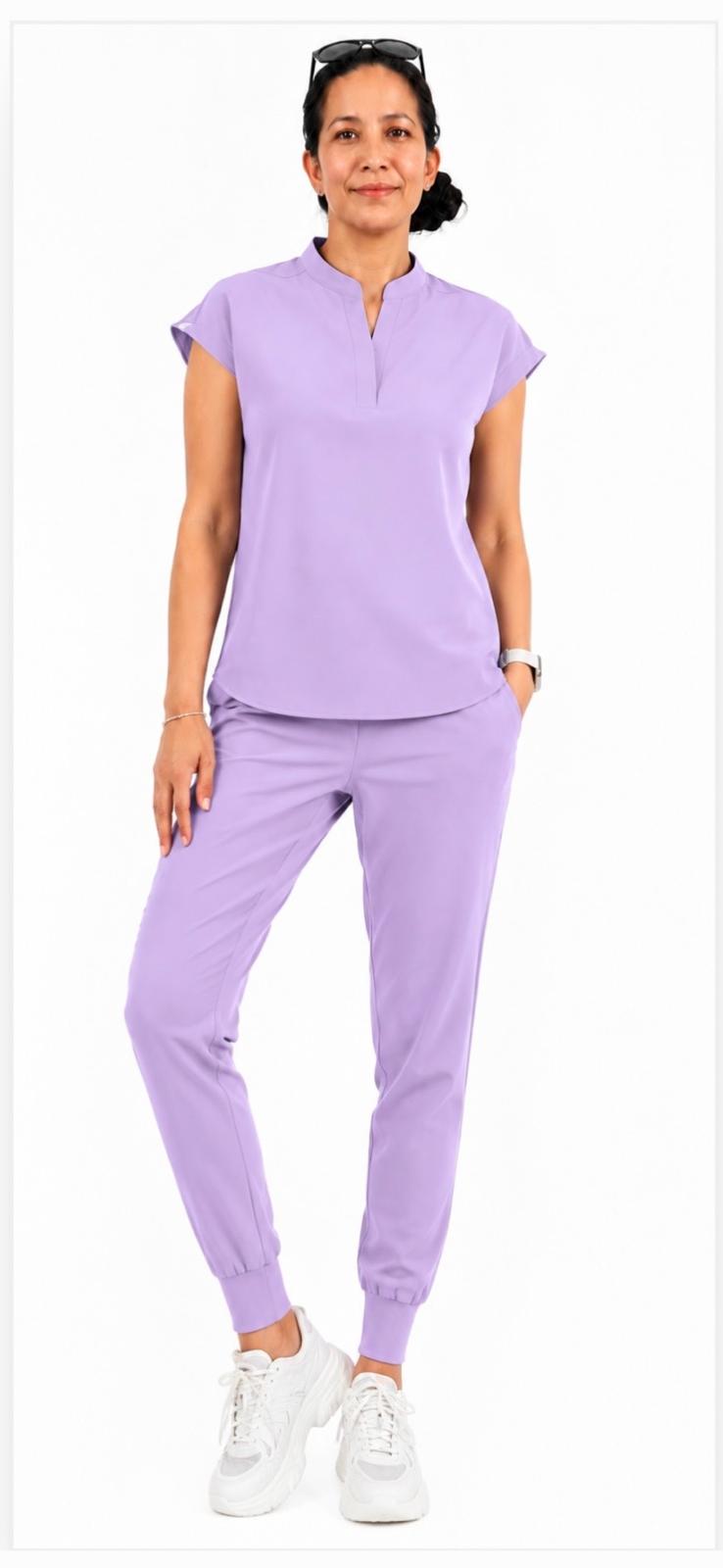 A woman modeling a matching lavender scrub set consisting of a short-sleeve mock-neck top and jogger pants, paired with white sneakers, against a plain white background.