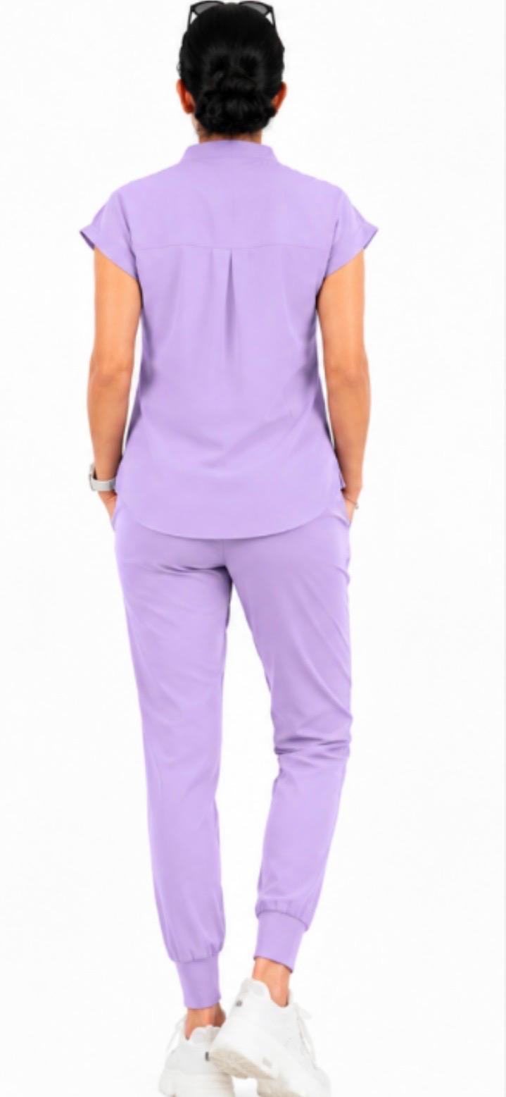 A person shown from the back wearing a light purple scrub set with short-sleeve top and matching pants, paired with white sneakers against a plain white background.